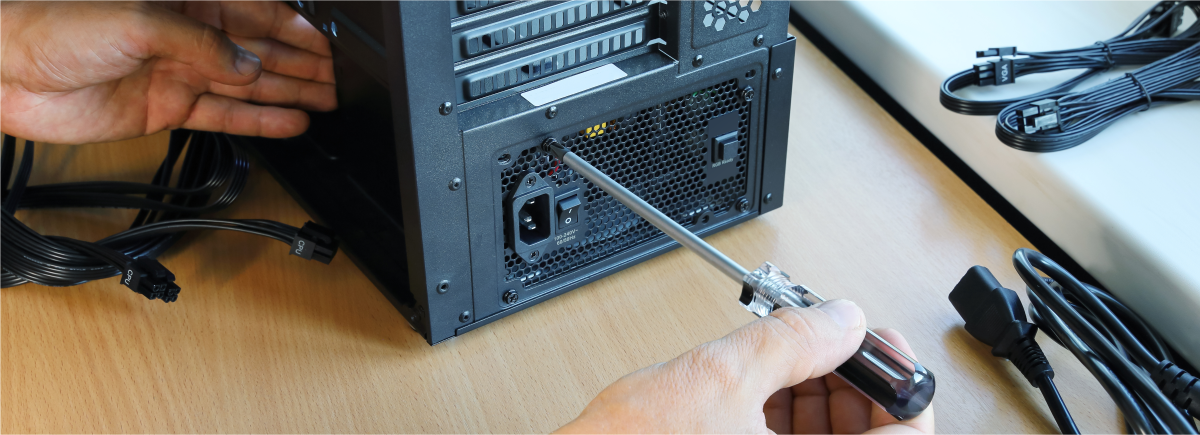 person with a screwdriver screws the black ATX power supply to the computer case