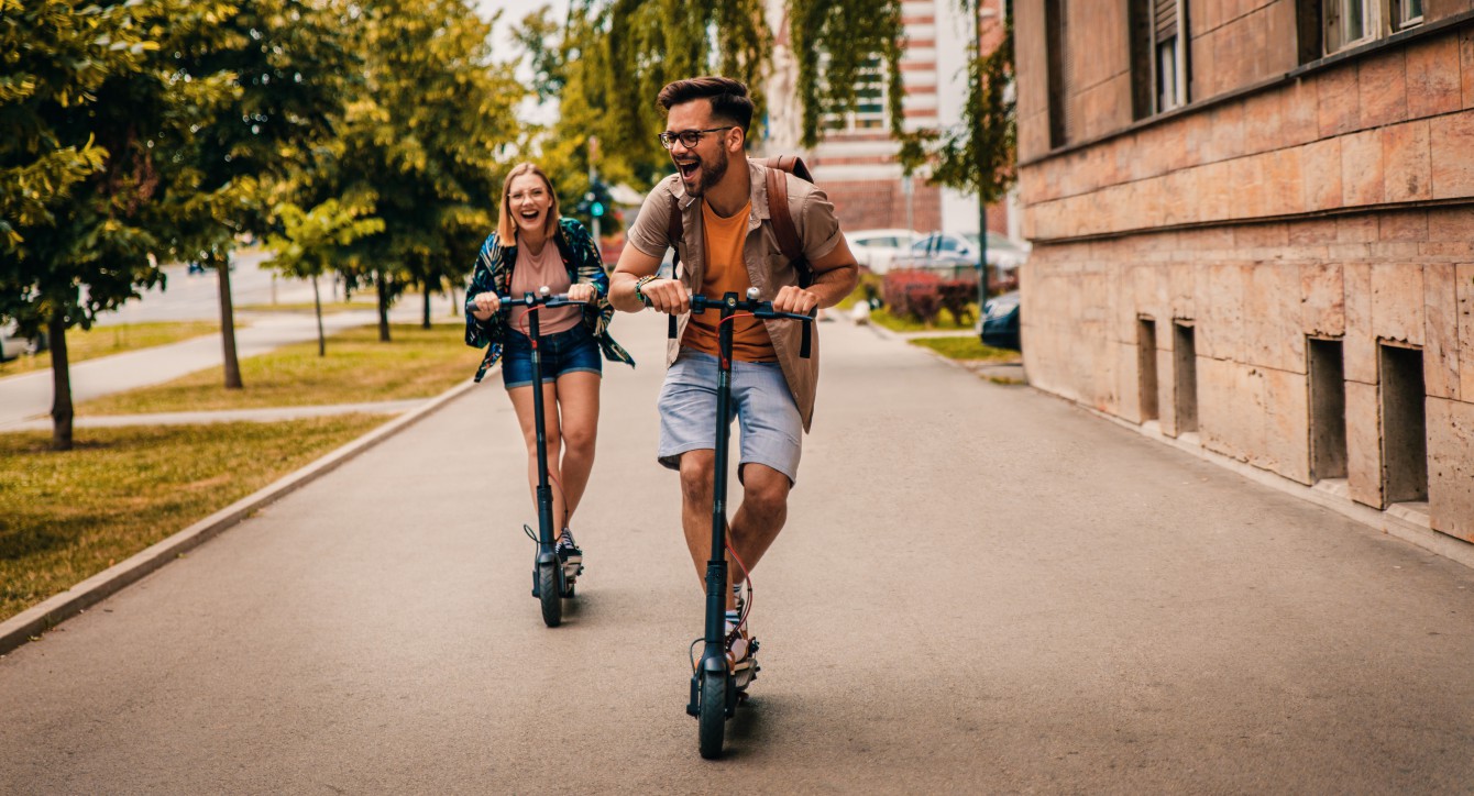  smiling couple racing through the city on xiaomi electric scooters